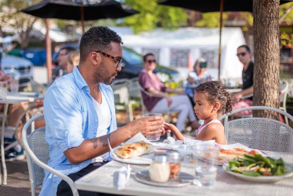 A man and his daughter sit at an outdoor table, eating.