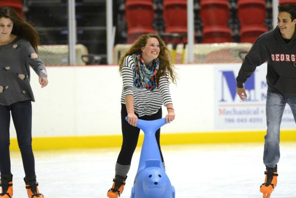 Three individuals ice skating at The Classic Center rink, one using a blue skating aid while the others glide on the ice.