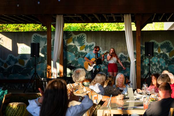 Live music performance at Hotel Indigo Athens Patio featuring a guitarist and vocalist under a mural-covered wooden pavilion with seated guests.
